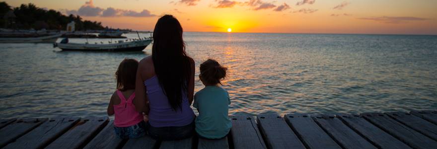 mãe e filhos observando o por do sol de um deck