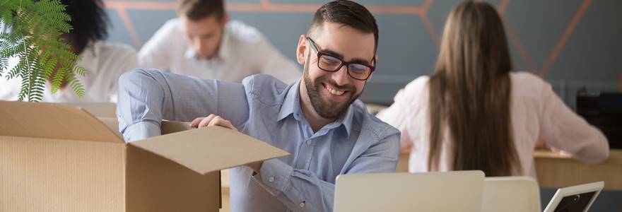 Smiling,New,Male,Employee,Unpacking,Box,With,Belongings,At,Workplace,